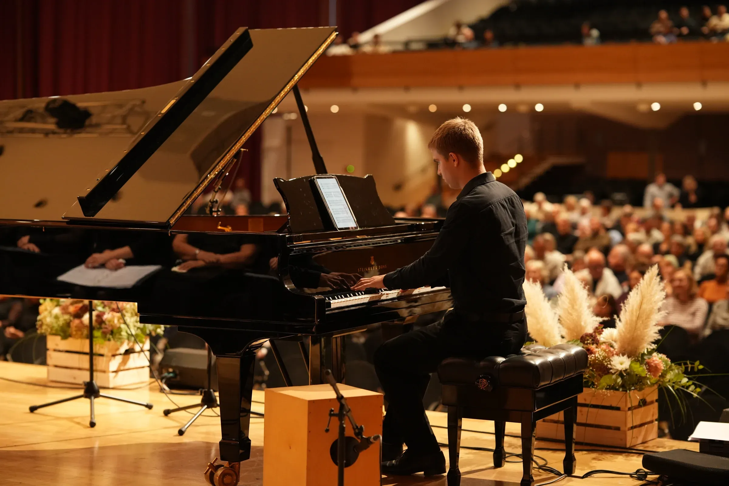 Ein junger Pianist spielt am Flügel, dahinter der vollbesetzte Konzertsaal.