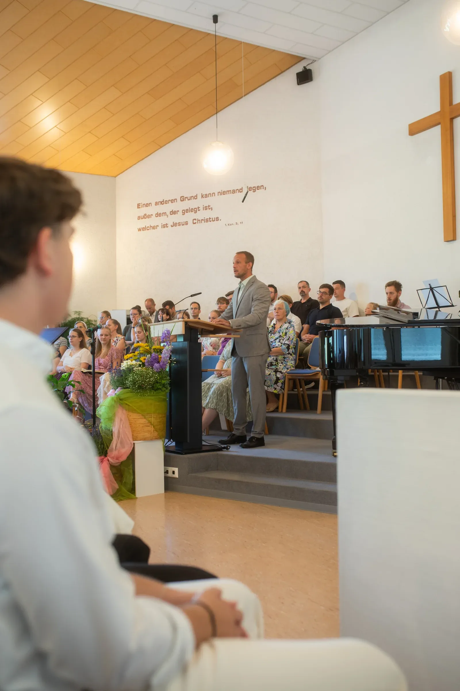 Taufgottesdienst: Blick über Blumen zum Rednerpult, dahinter die Gemeinde.